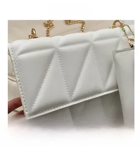 Nahaufnahme der weißen gesteppten Ledertextur mit goldener Kette und Mini-Taschenanhänger