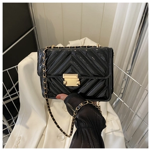 Detail of black patent leather crossbody bag with V-quilted stitching and gold metal clasp