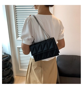 Detail of black crossbody bag with geometric triangle quilting and silver chain strap