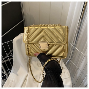Macro detail of golden chevron quilted leather bag with square metallic lock and chain strap