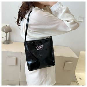 Close-up of black patent leather shoulder bag with pink butterfly embroidery detail