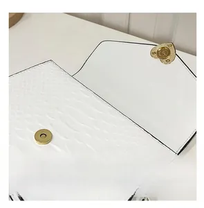 Detail of white crocodile pattern bag featuring a gold heart-shaped metal magnetic closure