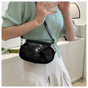 Sac bandoulière ovale noir avec texture crocodile et fermoir doré porté par le modèle
