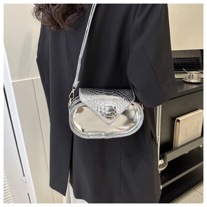 Gros plan d'un sac ovale argenté avec texture serpent porté sur un blazer noir chic
