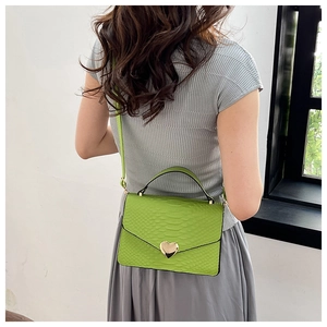 Detail of green crocodile pattern bag with golden heart-shaped clasp and top handle