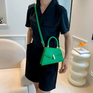 Modern asymmetric bright green leather handbag with gold clasp shown on a fashion model