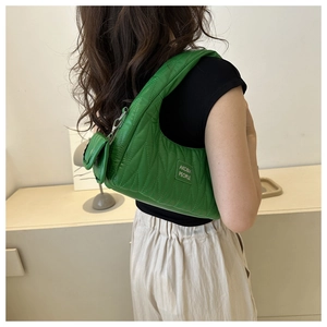 Sac sous le bras froncé vert avec mini pochette porté à l'épaule sous une lumière douce