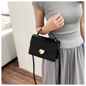 Detail of crocodile pattern handbag featuring a gold heart-shaped rotating lock closure