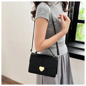 Detail of black faux snakeskin handbag with a gold heart-shaped metal buckle on a shoulder strap