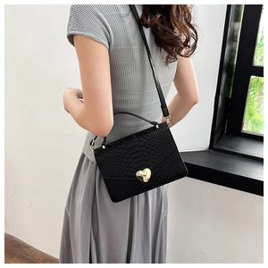 Detail of black crocodile texture handbag with a gold heart-shaped metal lock and strap
