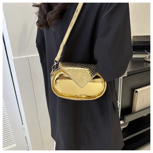 Détail du sac à bandoulière ovale doré avec texture crocodile porté sur une veste noire