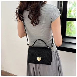 Detail of a black snake-embossed crossbody bag with a gold heart lock on a female model