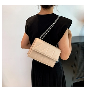 Detail of beige quilted crossbody bag with silver chain strap and geometric pattern