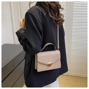 Pink faux leather handbag featuring snakeskin texture and a gold heart lock on a blazer