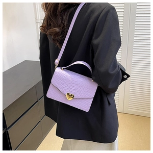Detailed view of a purple faux-snake skin crossbody bag with a gold heart clasp on a model