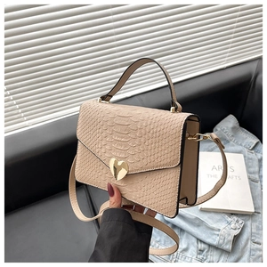 Detail of beige crocodile pattern handbag with a golden heart-shaped metal buckle