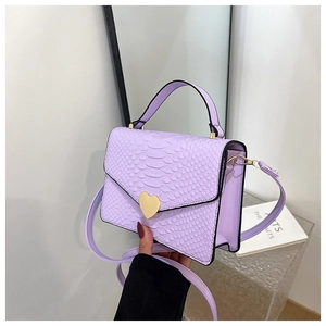 Detail of lavender crocodile pattern handbag with golden heart clasp and top handle