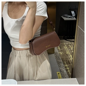 Detail of dark brown crocodile-embossed leather underarm bag with gold logo and knot strap