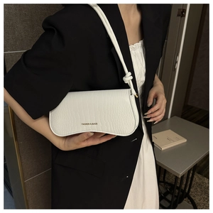Detail of white crocodile pattern underarm bag with knot strap on a model's shoulder