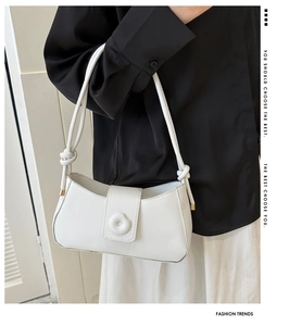 Detail shot of white minimalist baguette bag featuring knot strap and smooth leather texture