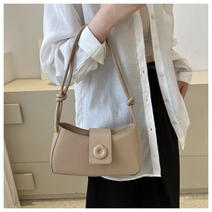 Detail of beige leather underarm bag featuring a round gold clasp and knotted strap design