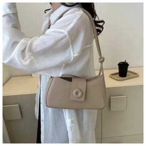 Detailed view of beige leather underarm bag with a unique circular 3D buckle closure