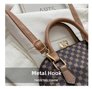 Dettaglio del gancio dorato e cuciture su borsa a conchiglia retrò con motivo monogram