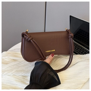 Detail of dark brown faux leather baguette bag with crocodile texture and knotted strap