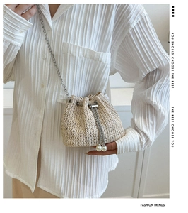 Détail d'un sac seau en paille avec motif en V, cordon en perles et chaîne en métal
