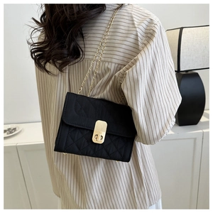 Close-up of black quilted shoulder bag with gold chain strap worn by a female model