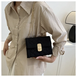 Close-up of black quilted shoulder bag with gold chain strap and metal lock closure