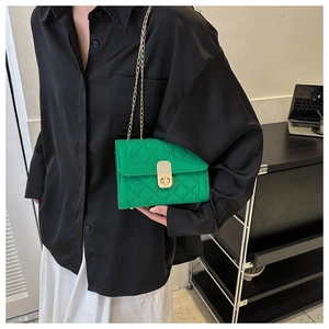 Close-up of green quilted small square bag featuring a gold metal twist lock and chain strap