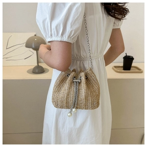 Détail du sac seau en paille tressée avec chaîne en métal argenté et cordon en perles