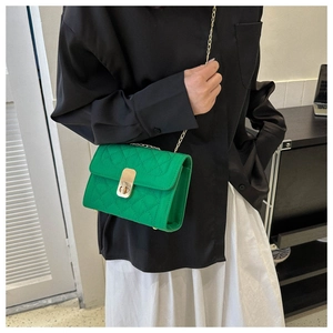 Close-up of green quilted shoulder bag with gold chain and metal lock on a model