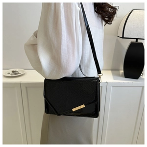 Zwarte crossbody tas met krokodillenpatroon, gouden sluiting en schouderband op model
