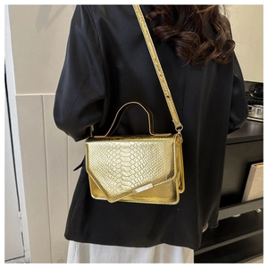 Detail van gouden handtas met krokodillenpatroon, asymmetrische flap en glans