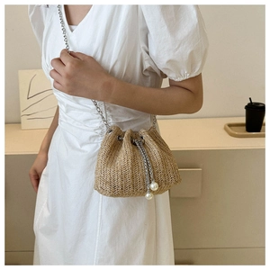 Détail du sac seau en paille avec fermeture à cordon et pendentifs en perles élégants