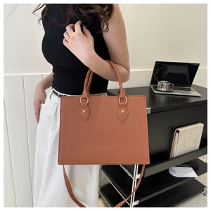 Brown Saffiano leather tote bag held by a model in a modern office business setting