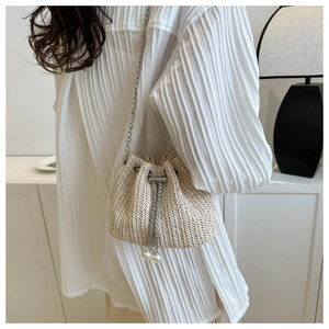 Détail du sac seau en paille tressée avec chaîne argentée et cordon en perles