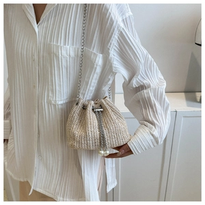 Détail du sac seau en paille avec bandoulière chaîne et grandes perles décoratives