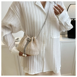 Détail du sac seau en paille avec breloques perles et bandoulière chaîne sur modèle
