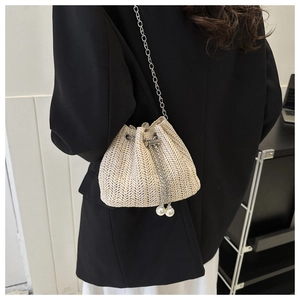 Détail du sac seau en paille tressée crème avec chaîne argentée et cordon en perles