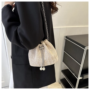 Détail du sac seau en paille avec chaîne dorée et cordon en perles sur un blazer noir