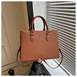 Brown Saffiano tote bag detail showing dual handles and golden hardware with a long strap