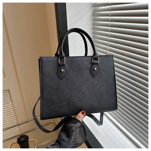 Detail of black Saffiano leather tote bag featuring golden metal rivets and dual handles