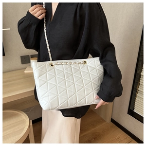 Detailed macro view of white quilted tote bag featuring golden metal chain straps