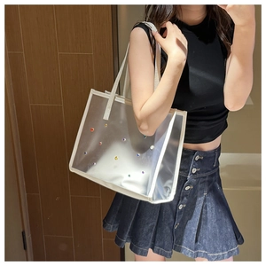 Detail of transparent PVC tote bag featuring colorful rhinestones and white leather straps