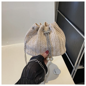 Détail du sac seau en paille beige avec tissage en V, breloque perle et bandoulière chaîne