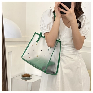 Detailed close-up of a semi-transparent PVC tote bag with green leather trim and colorful gems