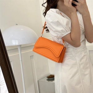 Minimalistische feloranje schoudertas met golfstiksels en gouden details aan een model
